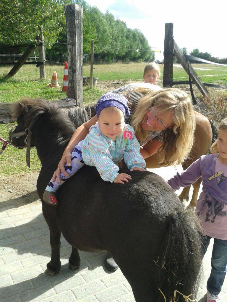 Ein Kleinkind sitzt glücklich auf dem Rücken eines Pferdes und wird von einer Frau festgehalten.